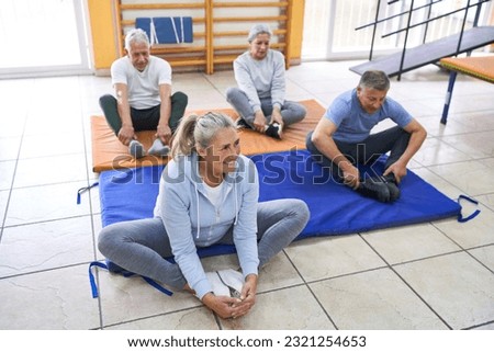 Smiling senior woman and man practicing cobbler pose during exercise class in rehab center Royalty-Free Stock Photo #2321254653