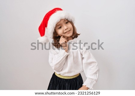 Little hispanic girl wearing christmas hat smiling looking confident at the camera with crossed arms and hand on chin. thinking positive. 