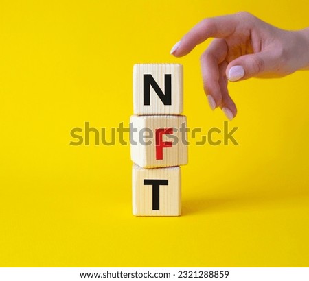 NFT - non-fungible token symbol. Concept word NFT on wooden cubes. Businessman hand. Beautiful yellow background. Business and NFT concept. Copy space.