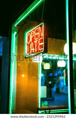 A vertical shot of an open late sign hanging in the window with neon light