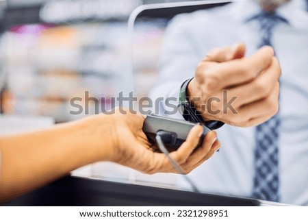 The focus is on a male with a smartwatch paying a bill at the counter in a store. Royalty-Free Stock Photo #2321298951