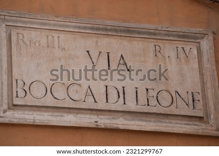 A horizontal shot of a beige old street address sign of Via Bocca di Leone on a wall in Rome