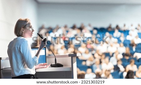 Female speaker giving a talk on corporate business conference. Unrecognizable people in audience at conference hall. Business and Entrepreneurship event