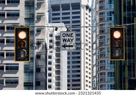 A one way sign hanging between two traffic lights on high buildings background