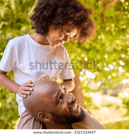 Father And Son In Summer Garden With Boy Riding On Dads Shoulders