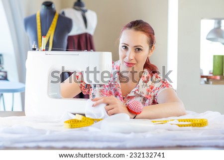 Young attractive needlewoman at studio working with sewing machine