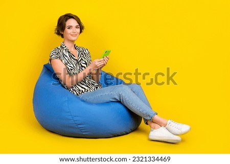 Full length photo of pretty shiny lady wear animal print shirt bean bag texting iphone apple gadget empty space isolated yellow color background