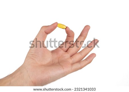 Man's hand holding a yellow pill of omega 3 isolated on a white background.