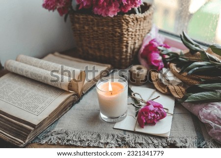 Burning candle and pink peonies, vintage aesthetic.