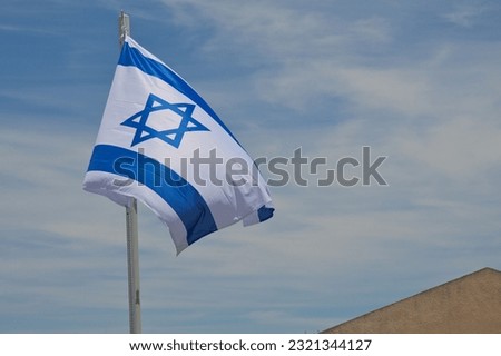 The flag of Israel on pole flutters in wind under blue sky. Israeli flag with the star of David