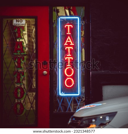 The neon sign of a tattoo shop on the street.