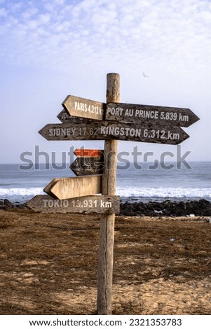 A closeup of wooden direction signs on a road with a view of a sea under the blue cloudy sky