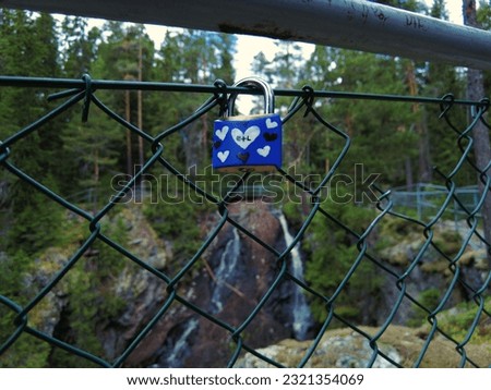 Couple in love confirm with padlock on fence the eternal love symbol. In the background a waterfall and forest, shallow depth of field