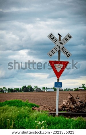 A vertical shot of railroad crossing and yield signs in a rural area in cloudy sky background