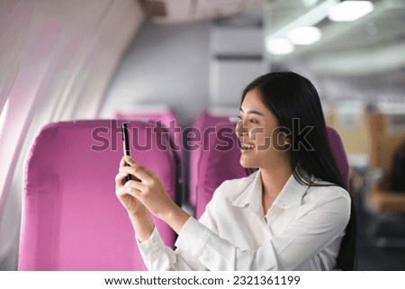 Young asian woman passenger taking photo from the window of the airplane during flight.