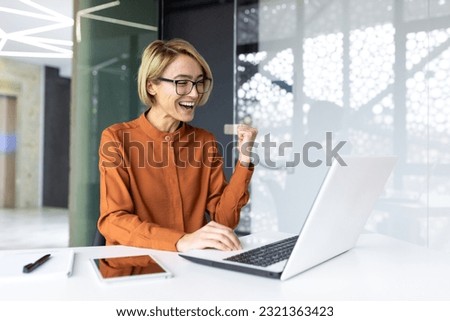 Successful businesswoman inside the office is satisfied with the results of the achievement, the employee received a good completed technical task, holds her hands up in a gesture of triumph Royalty-Free Stock Photo #2321363423