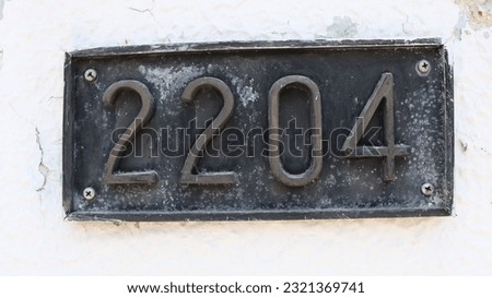 A close-up shot of a rustic metallic number 2204 on white wall background.
