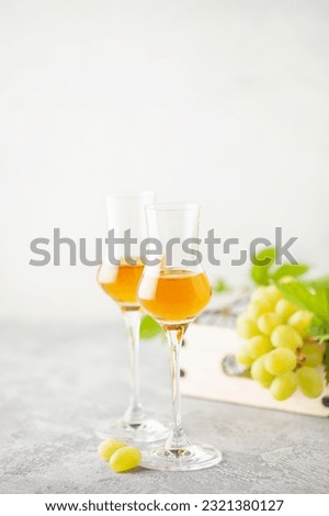 Gold grappa in grappas wineglasses and fresh grapes on the gray background. Alcohol concept Royalty-Free Stock Photo #2321380127