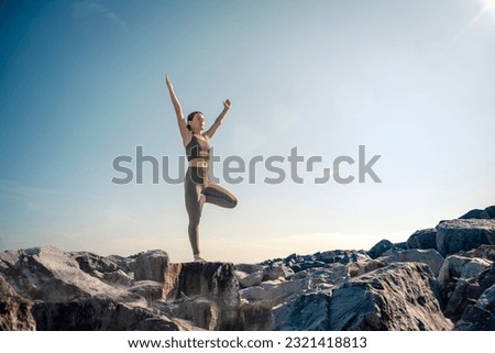 Woman doing a yoga tree pose on top of rocks at sunrise, sunset. Royalty-Free Stock Photo #2321418813