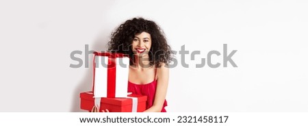 Beautiful birthday girl with curly hair, holding bday gifts and smiling happy, celebrating, standing against white background.
