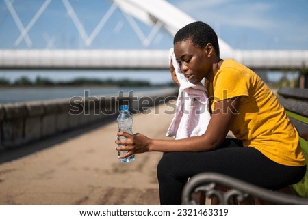 Exhausted woman after exercise drinking water and wiping sweat with towel. Royalty-Free Stock Photo #2321463319