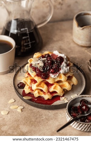 Belgian waffles with sour cream, cherry jam and almond petals topping and coffee on beige kitchen background. Sweet morning breakfast Royalty-Free Stock Photo #2321467475