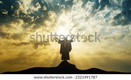 Silhouette of Jesus praying with raised hands on a mount with mystic clouds behind Him. Royalty-Free Stock Photo #2321491787