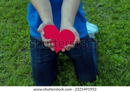 Young man on kneels  in the park holding a red heart