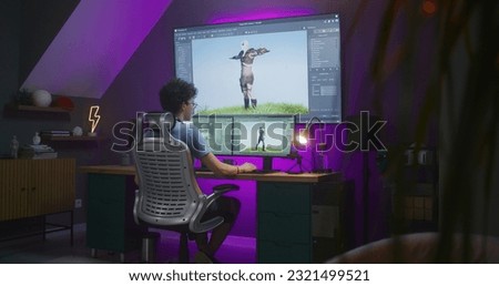 Young 3D designer creates animation for video game character, works remotely from home late night on computer and big digital screen with professional software interface for 3D modeling and design. Royalty-Free Stock Photo #2321499521