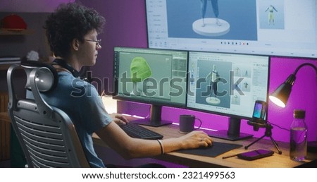 Young 3D designer creates video game character or clothes, works remotely from home on computer and big digital screen with professional software interface and tools for 3D modeling and design. Royalty-Free Stock Photo #2321499563