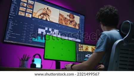 Young video maker edits movie about space mission, works at home office. Film footage and software interface with tools and sound tracks on big digital screen. Computer monitor with green screen.