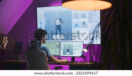 Young 3D designer creates video game character or clothes, works remotely from home in the evening on computer and big digital screen with professional software interface for 3D modeling and design. Royalty-Free Stock Photo #2321499617