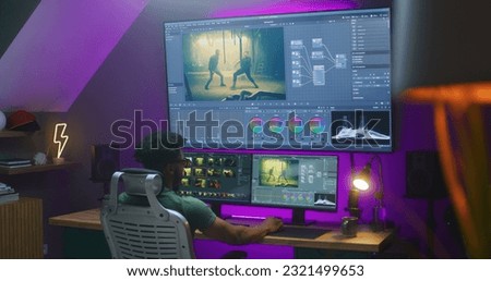 African American video maker edits action movie, makes color grading, works at home. Software interface with RGB tools and wheels on computer and big digital screen. Concept of film post production.
