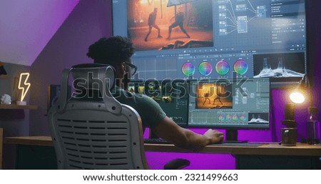 African American editor makes color correction, edits action movie, works at home. Software interface with RGB tools and wheels on computer and big digital screen. Concept of film post production. Royalty-Free Stock Photo #2321499663