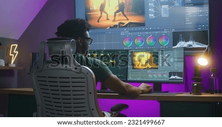 African American editor makes color correction, edits action movie, works at home. Software interface with RGB tools and wheels on computer and big digital screen. Concept of film post production.