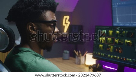 African American colorist edits action movie, makes color correction, works at home. Program interface with RGB tools and wheels on computer and big digital screen. Concept of film post production.