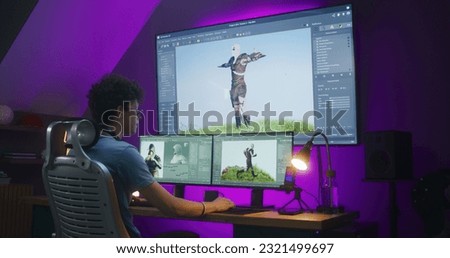 Young creative 3D designer creates video game character or animation, works remotely at home office. Computer and big digital screen with professional software interface for 3D modeling and design. Royalty-Free Stock Photo #2321499697