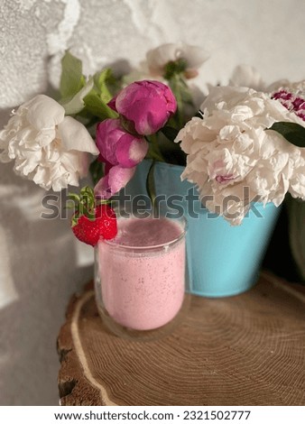 a glass of cold strawberry smoothie and a vase of flowers