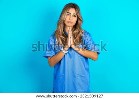 Positive young beautiful doctor woman smiles happily, glad to receive pleasant news from interlocutor, keeps palms together, People emotions concept.