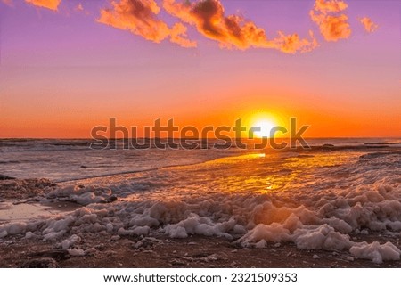 Sun setting on the horizon over the sea and the beach covered with golden foam.
