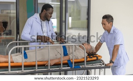 Team of nurses or rescuers with an African doctor uses stretcher to carry an elderly patient to an emergency room Royalty-Free Stock Photo #2321523293