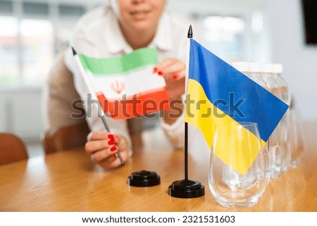 Unrecognizable woman preparing room for international negotiations and communication discussions of leaders. Lady sets miniatures flags of Ukraine and Iran on table. Unfocused shot