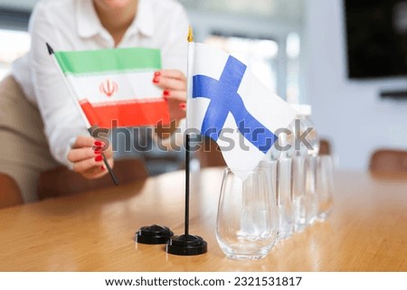 Young woman in business clothes puts flags of Iran and Finland on negotiating table in office