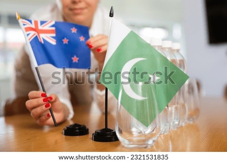 Young woman in business clothes puts flags of New Zealand and Pakistan on negotiating table in office