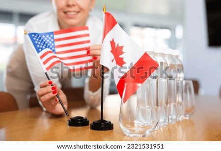 Young woman in business clothes puts flags of USA and Canada on negotiating table in office..