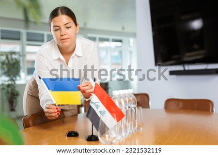 Female secretary places flags of the Iraq and Ukrain flag on the table before the negotiations of top political figures
