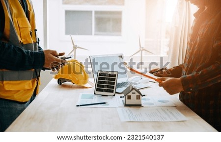 Engineer and contractor pointing at model house and solar panels with their hands To jointly design the use of renewable energy, both wind and solar energy. concept of renewable energy