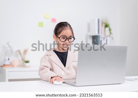 Little business lady Asia. Cute little girl in glasses and formalwear sitting at the table and using laptop
