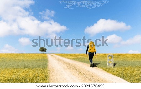 Camino de Santiago - A young pilgrim with a yellow backpack, walking alone in Saint James way, on a pilgrimage to Santiago de Compostela, Spain - Selective focus Royalty-Free Stock Photo #2321570453