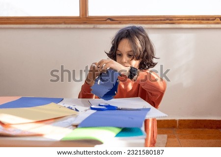 The child makes a snowflake out of colored paper. the boy cuts a snowflake out of blue paper with scissors. children's creativity. Royalty-Free Stock Photo #2321580187